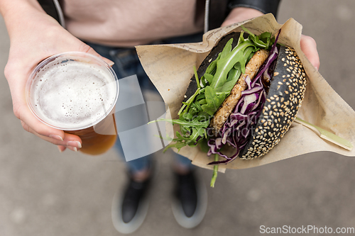 Image of Close up of woman hands holding delicious organic salmon vegetarian burger and homebrewed IPA beer on open air beer an burger urban street food festival in Ljubljana, Slovenia.