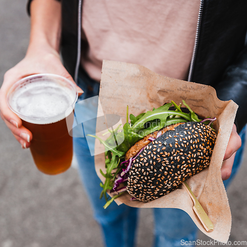 Image of Close up of woman hands holding delicious organic salmon vegetarian burger and homebrewed IPA beer on open air beer an burger urban street food festival in Ljubljana, Slovenia.