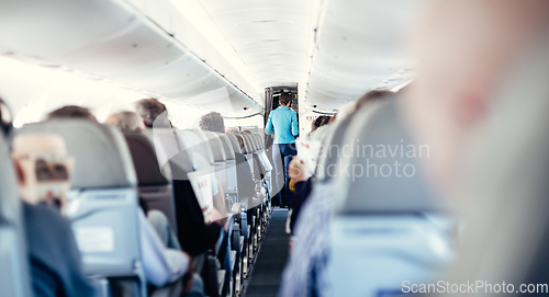 Image of Interior of airplane with passengers on seats and stewardess in uniform walking the aisle, serving people. Commercial economy flight service concept.