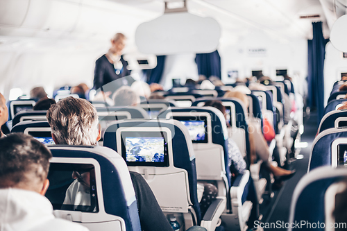 Image of Interior of airplane with passengers on seats and stewardess in uniform walking the aisle, serving people. Commercial economy flight service concept.