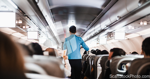 Image of Interior of airplane with passengers on seats and stewardess in uniform walking the aisle, serving people. Commercial economy flight service concept.