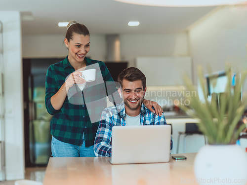 Image of A young married couple is talking to parents, family and friends on a video call via a laptop while sitting in the living room of their modern house