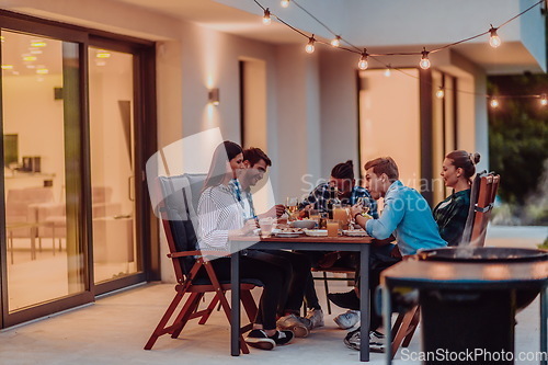 Image of A group of young diverse people having dinner on the terrace of a modern house in the evening. Fun for friends and family. Celebration of holidays, weddings with barbecue.