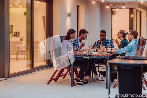 Image of A group of young diverse people having dinner on the terrace of a modern house in the evening. Fun for friends and family. Celebration of holidays, weddings with barbecue.