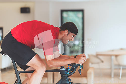 Image of A man riding a triathlon bike on a machine simulation in a modern living room. Training during pandemic conditions.