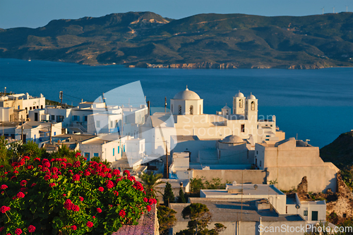 Image of View of Plaka village on Milos island over red geranium flowers on sunset in Greece