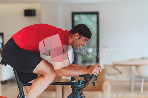 Image of A man riding a triathlon bike on a machine simulation in a modern living room. Training during pandemic conditions.