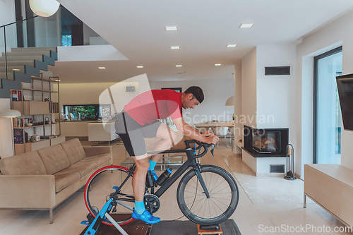 Image of A man riding a triathlon bike on a machine simulation in a modern living room. Training during pandemic conditions.