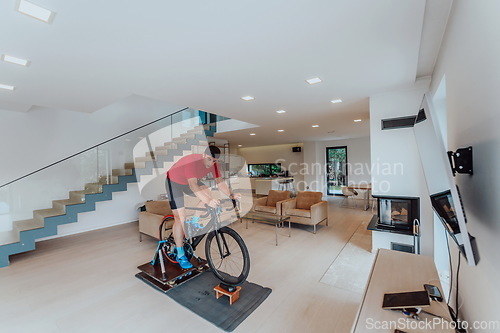 Image of A man riding a triathlon bike on a machine simulation in a modern living room. Training during pandemic conditions.