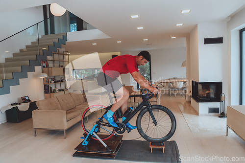 Image of A man riding a triathlon bike on a machine simulation in a modern living room. Training during pandemic conditions.