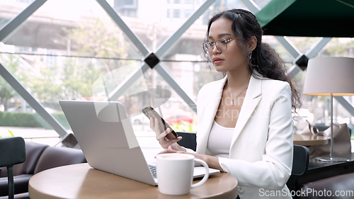 Image of A busy businesswoman using laptop and having coffee