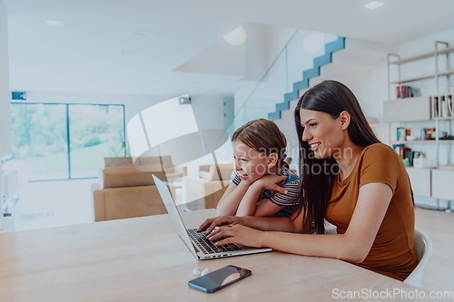 Image of Mother with her daughter talking on laptop with family and friends while sitting in modern living room of big house