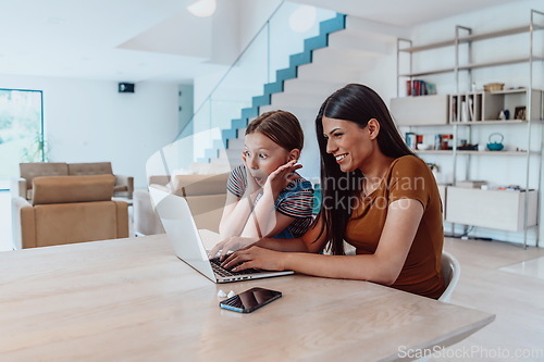 Image of Mother with her daughter talking on laptop with family and friends while sitting in modern living room of big house