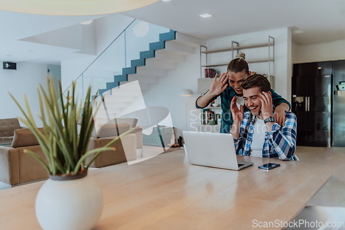 Image of A young married couple is talking to parents, family and friends on a video call via a laptop while sitting in the living room of their modern house