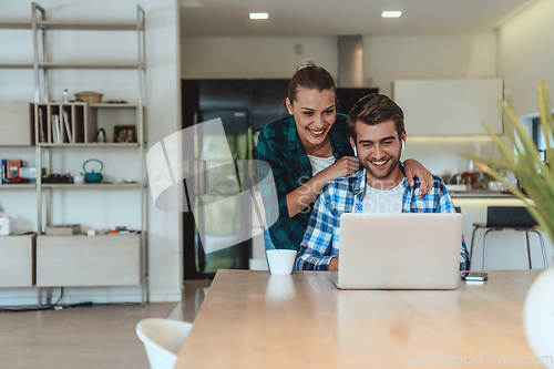 Image of A young married couple is talking to parents, family and friends on a video call via a laptop while sitting in the living room of their modern house