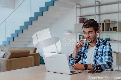 Image of The man sitting at a table in a modern living room, with headphones using a laptop for business video chat, conversation with friends and entertainment