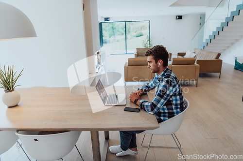 Image of The man sitting at a table in a modern living room, with headphones using a laptop for business video chat, conversation with friends and entertainment