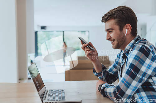 Image of The man sitting at a table in a modern living room, using a smartphone and laptop for business video chat, conversation with friends and entertainment