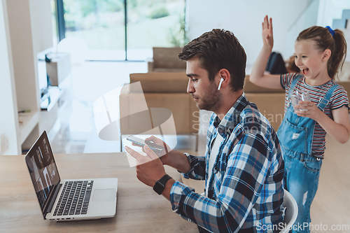 Image of The man sitting at a table in a modern living room, with headphones using a laptop and smartphone for business video chat, conversation with friends and entertainment