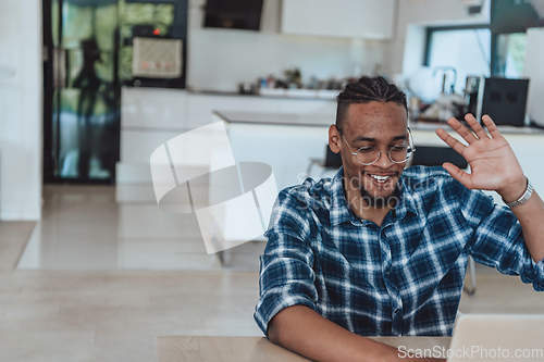 Image of African American man in glasses sitting at a table in a modern living room, using a laptop for business video chat, conversation with friends and entertainment