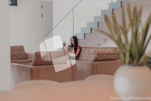 Image of Woman using smartphone for video call while sitting in modern house