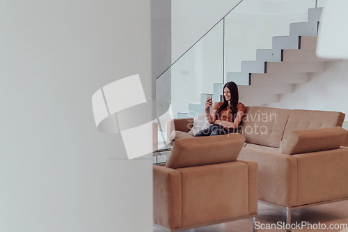 Image of Woman using smartphone for video call while sitting in modern house