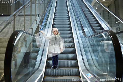 Image of From below shot of girl standing on moving stairs in terminal.
