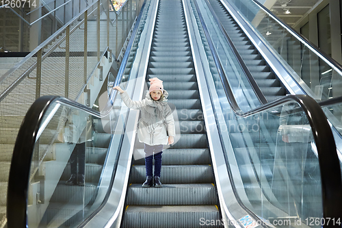 Image of From below shot of girl standing on moving stairs in terminal.