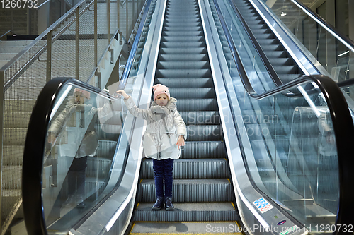 Image of From below shot of girl standing on moving stairs in terminal.