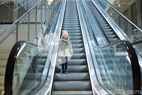 Image of From below shot of girl standing on moving stairs in terminal.