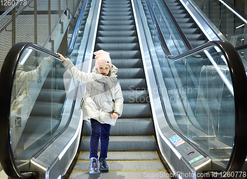 Image of From below shot of girl standing on moving stairs in terminal.