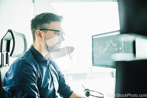 Image of Stock broker trading online watching charts and data analyses on multiple computer screens.