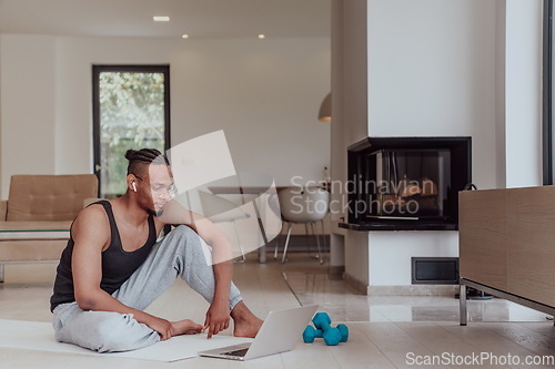 Image of Training At Home. Sporty man doing training while watching online tutorial on laptop, exercising in living room, free space