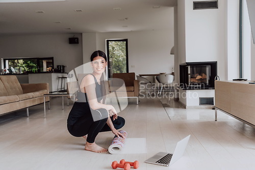 Image of A young woman in sports clothes preparing sports equipment for online training in her living room