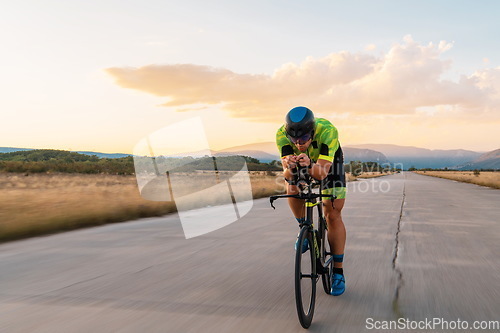 Image of Triathlete riding his bicycle during sunset, preparing for a marathon. The warm colors of the sky provide a beautiful backdrop for his determined and focused effort.