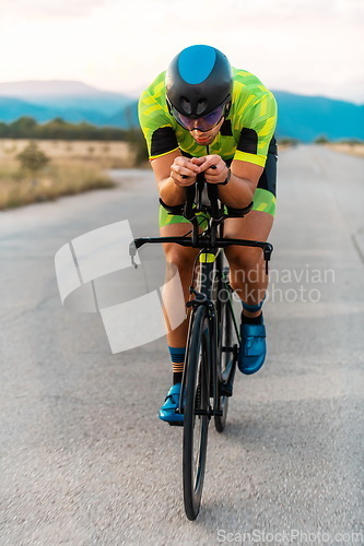 Image of Triathlete riding his bicycle during sunset, preparing for a marathon. The warm colors of the sky provide a beautiful backdrop for his determined and focused effort.