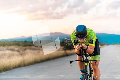 Image of Triathlete riding his bicycle during sunset, preparing for a marathon. The warm colors of the sky provide a beautiful backdrop for his determined and focused effort.