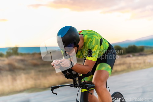 Image of Triathlete riding his bicycle during sunset, preparing for a marathon. The warm colors of the sky provide a beautiful backdrop for his determined and focused effort.