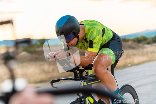 Image of Triathlete riding his bicycle during sunset, preparing for a marathon. The warm colors of the sky provide a beautiful backdrop for his determined and focused effort.