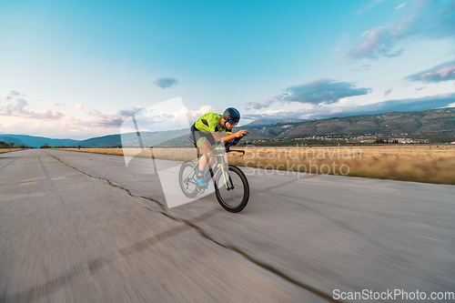 Image of Triathlete riding his bicycle during sunset, preparing for a marathon. The warm colors of the sky provide a beautiful backdrop for his determined and focused effort.