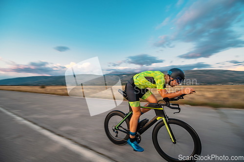 Image of Triathlete riding his bicycle during sunset, preparing for a marathon. The warm colors of the sky provide a beautiful backdrop for his determined and focused effort.