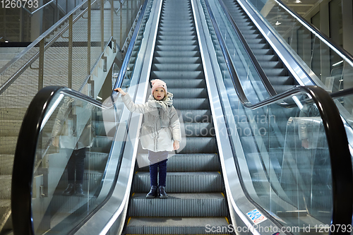 Image of From below shot of girl standing on moving stairs in terminal.