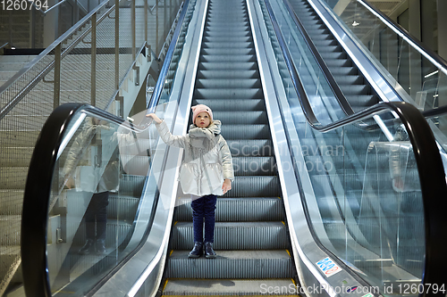 Image of From below shot of girl standing on moving stairs in terminal.