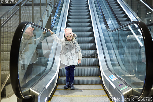 Image of From below shot of girl standing on moving stairs in terminal.