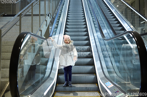 Image of From below shot of girl standing on moving stairs in terminal.