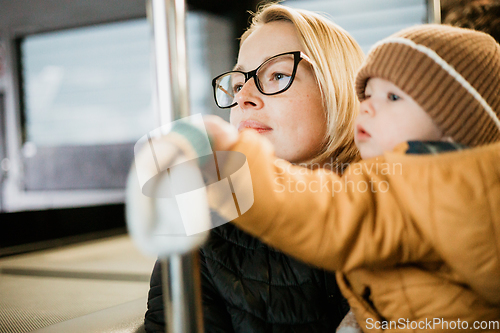 Image of Mother carries her child while standing and holding on to the bus. Mom holding her infant baby boy in her arms while riding in a public transportation. Cute toddler boy traveling with his mother.