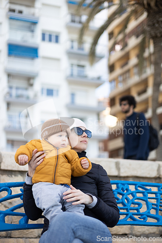 Image of Young mother with her cute infant baby boy child on bench in city park.