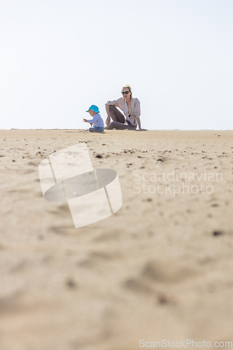 Image of Mother playing his infant baby boy son on sandy beach enjoying summer vacationson on Lanzarote island, Spain. Family travel and vacations concept.