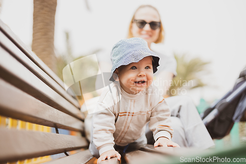 Image of Young mother with her cute infant baby boy child on bench on urban children's playground on warm summer day.
