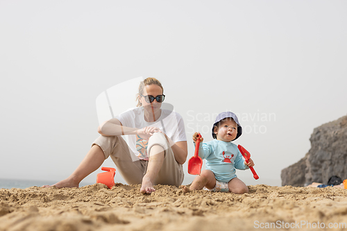 Image of Mother playing his infant baby boy son on sandy beach enjoying summer vacationson on Lanzarote island, Spain. Family travel and vacations concept.